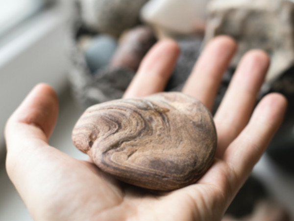 Eine Hand hält eine runde, gemusterte Steinplatte mit welligen Mustern.